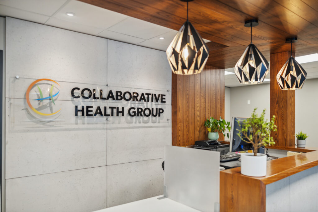 Reception area of Collaborative Health Group featuring pendant lights, wood paneling, potted plants, and the clinic’s logo displayed prominently on the wall.