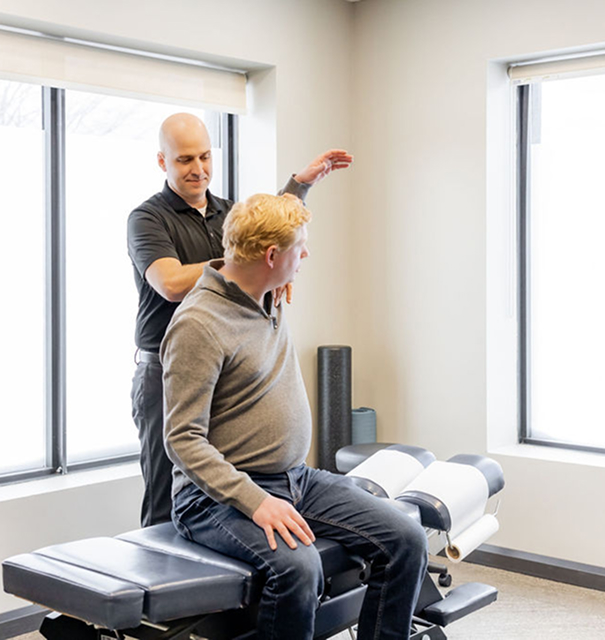Dr. Peter Wilson evaluating a client’s shoulder range of motion as they sit on an exam bench with one arm raised. Bright windows line the room.