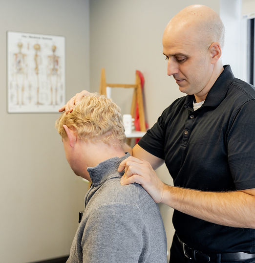 Dr. Peter Wilson assisting a client by gently pressing the top of their head during a posture or mobility evaluation in a chiropractic treatment room.