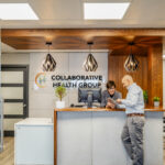 Elizabeth Adams-Sweet and Dr. Peter Wilson at the reception desk of Collaborative Health Group, smiling as they look at a tablet together. The setting conveys a sense of teamwork and approachability.