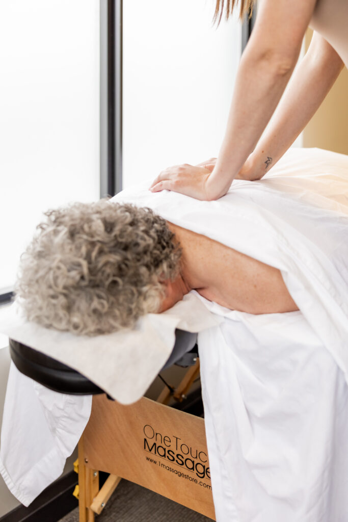 A patient receiving a massage while lying face down under a white sheet, with his curly hair visible. Rachel Cubitt's hands apply pressure to his back.